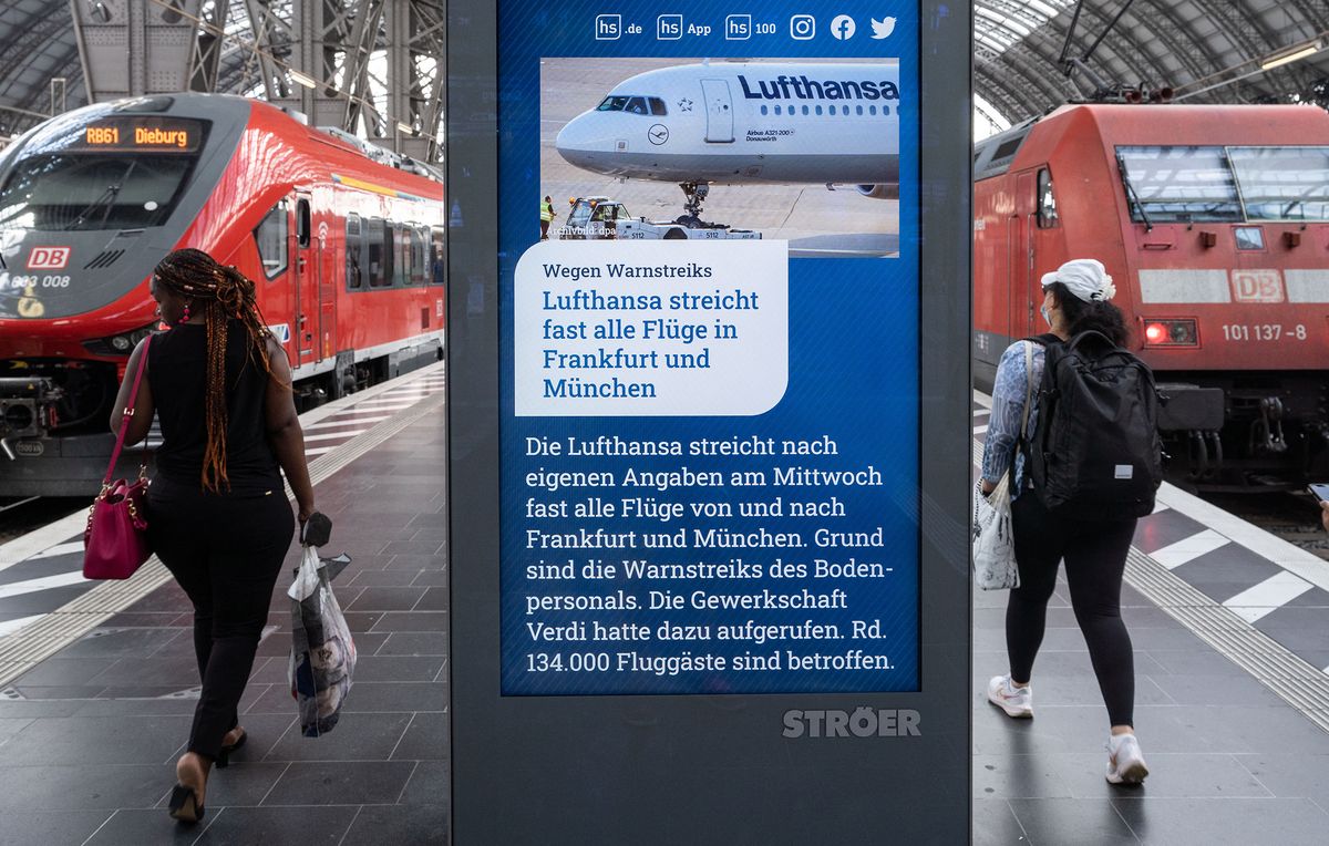 26 July 2022, Hessen, Frankfurt/Main: Rail passengers walk past an information screen in Frankfurt's main train station that reads "Lufthansa cancels almost all flights in Frankfurt and Munich" as a message. Lufthansa is canceling almost the entire flight schedule at its German hubs in Frankfurt and Munich on Wednesday (July 27, 2022) because of the Verdi warning strike. Photo: Frank Rumpenhorst/dpa (Photo by FRANK RUMPENHORST / DPA / dpa Picture-Alliance via AFP)