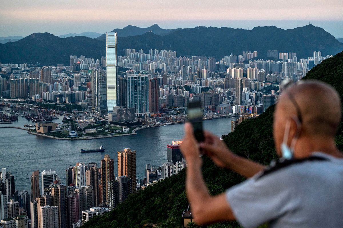 A man taking a photo with his phone of the Hong Kong and Kowloon Skyline on a mountain on July 13, 2022 in Hong Kong, China. (Photo by Vernon Yuen/NurPhoto) (Photo by Vernon Yuen / NurPhoto / NurPhoto via AFP)