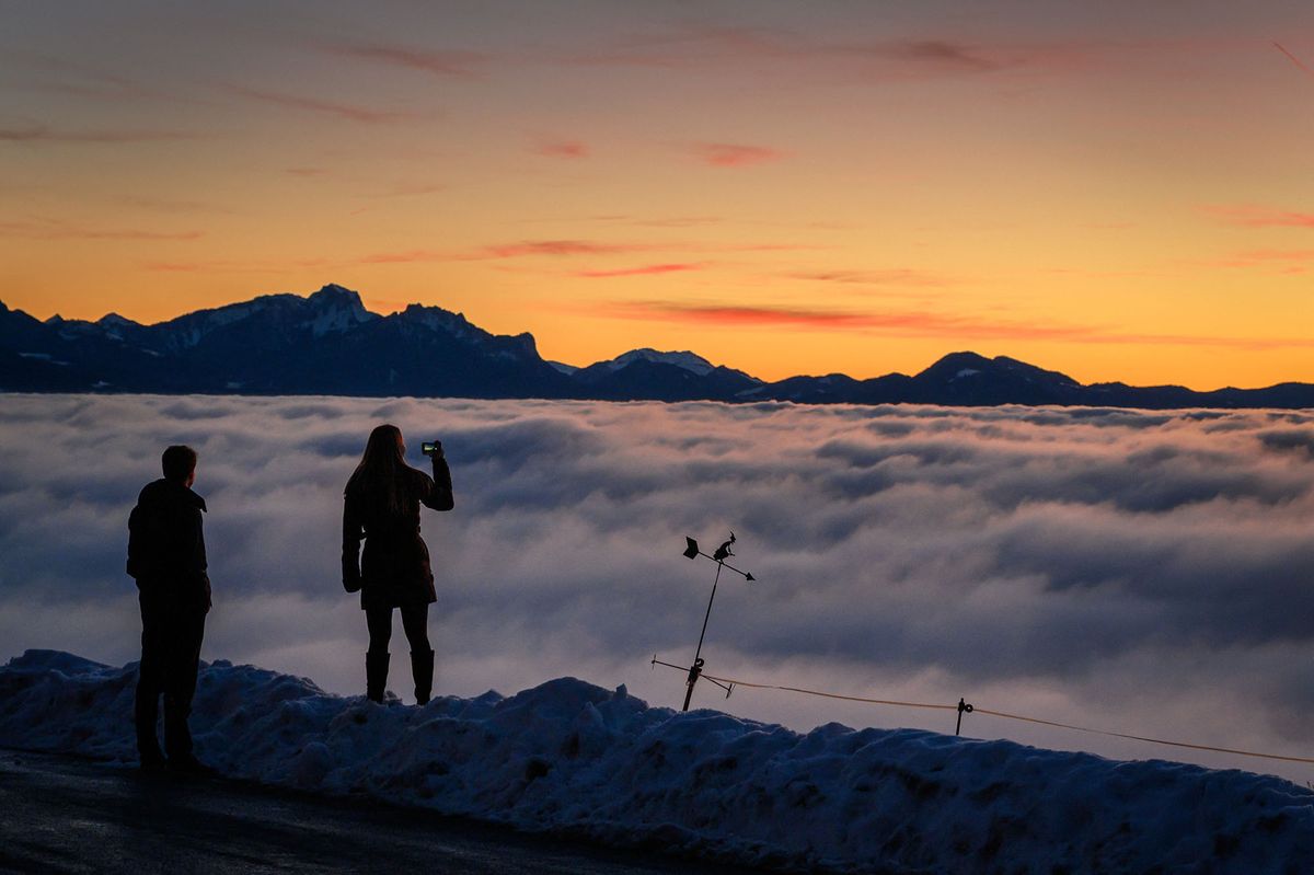 A couple is silhouetted with Alps surrounded by a sea of fog hanging above Lake Geneva in Mont de Gourze above Riez, Western Switzerland, after sunset on December 14, 2021. (Photo by Fabrice COFFRINI / AFP)
