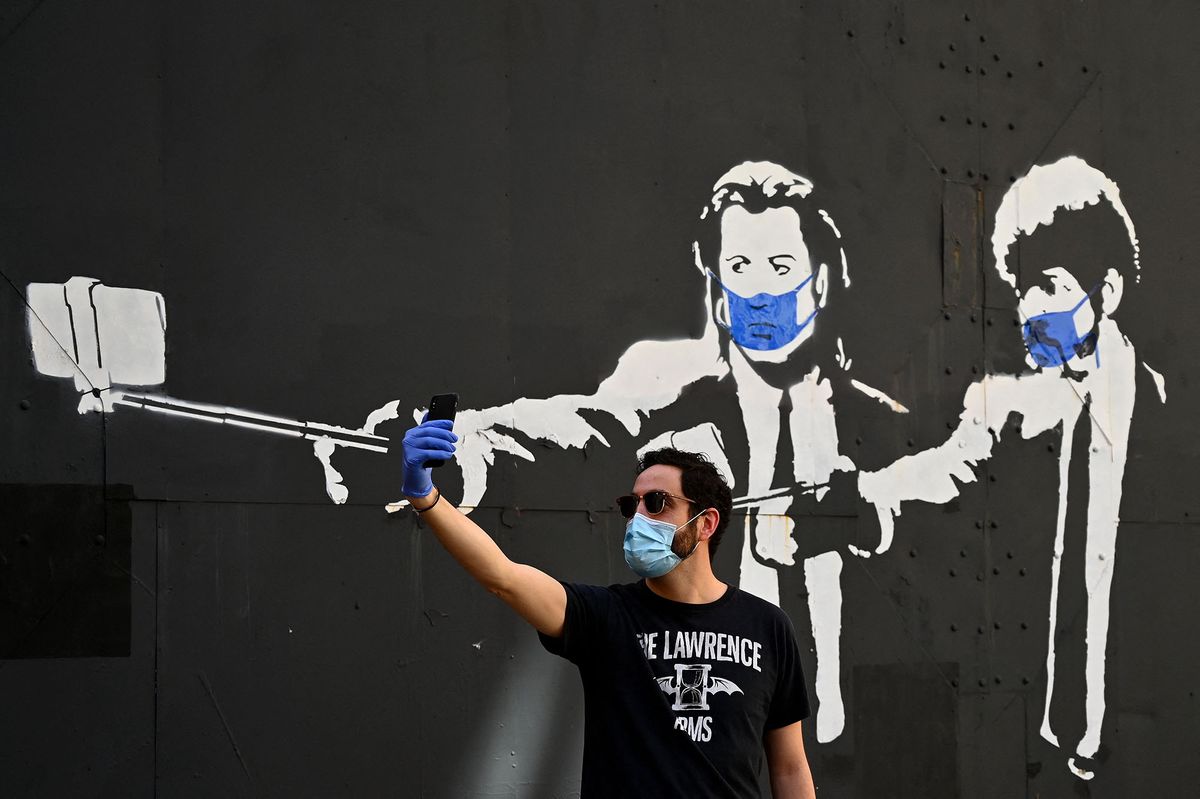 A man takes a selfie photo in front of a stencil graffiti depicting US actors John Travolta and Samuel L. Jackson in their roles of "Vincent Vega" and "Jules Winnfield" in Quentin Tarantino's "Pulp Fiction", wearing face masks, in Madrid on May 3, 2020 amid a national lockdown to prevent the spread of the COVID-19 disease. - Spain today counted another 164 coronavirus deaths, the lowest daily number in nearly seven weeks as the country begins to gradually lift its strict lockdown. The figures from the health ministry bring the total number of fatalities from the pandemic in Spain to 25,264 -- the fourth-highest after the United States, Italy and Britain. (Photo by Gabriel BOUYS / AFP)