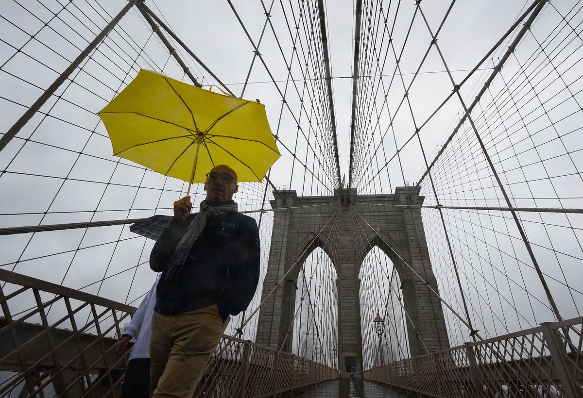 People carrying umbrellas walk across the Brooklyn Bridge in the rain in New York on June 22, 2022. (Photo by ANGELA WEISS / AFP)