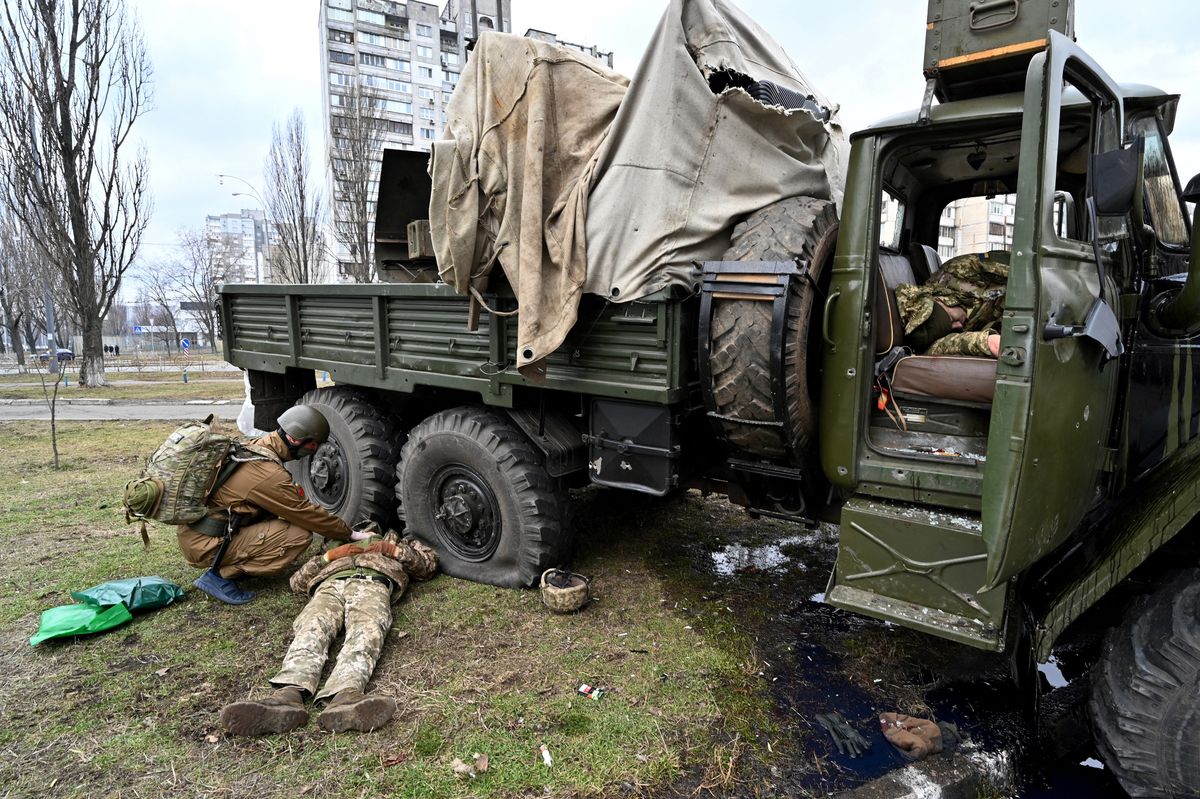 EDITORS NOTE: Graphic content / An Ukrainian military medic (L) examines the body of a Russian serviceman wearing a Ukranian service uniform lying beside a vehicle after he and members from a raiding party were shot during a skirmish in the Ukrainian capital of Kyiv on February 25, 2022, according to Ukrainian service personnel at the scene. - Russian forces are approaching Kyiv from the north and northeast, Ukraine's army said, with rising fears the capital could fall on the second day of Moscow's offensive. (Photo by Sergei SUPINSKY / AFP)