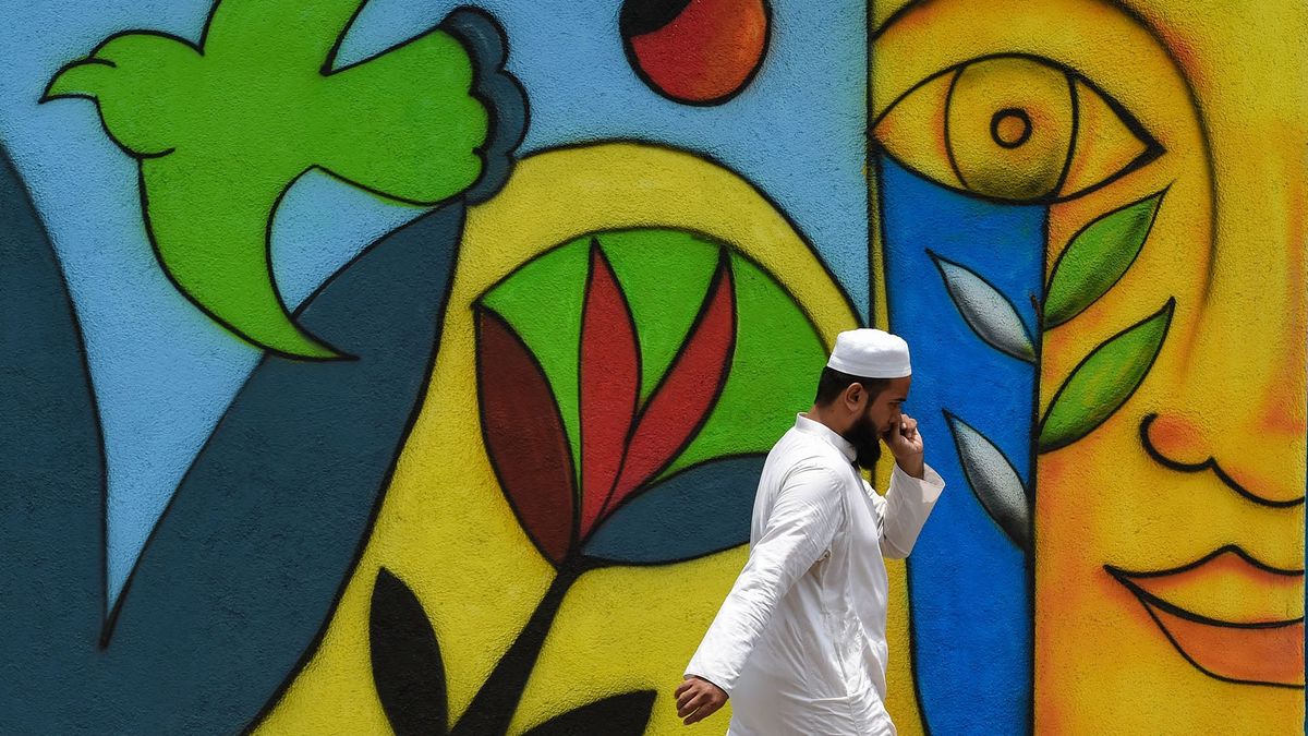A pedestrian speaks on a phone as he walks past a mural along a street in Mumbai on July 6, 2021. (Photo by Punit PARANJPE / AFP)