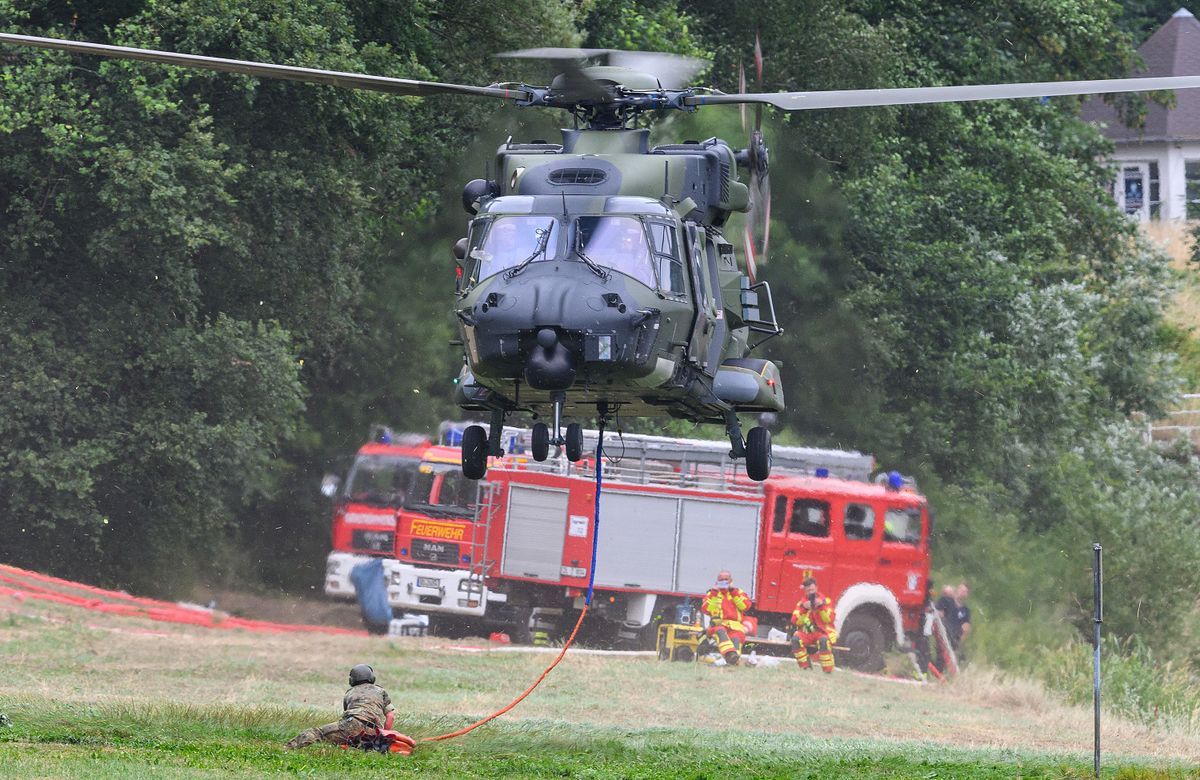 27 July 2022, Saxony, Schmilka: A Bundeswehr helicopter took off from the banks of the Elbe River with an external water tank to extinguish a fire in the erdőtűz, forestfire, német-cseh határ