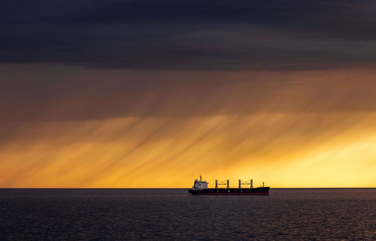 14 June 2022, Mecklenburg-Western Pomerania, Rostock: A cargo ship is lying in the roads outside the port of Rostock. On the horizon, rain clouds pass over the Baltic Sea in front of the low evening sun. Photo: Jens B¸ttner/dpa (Photo by JENS BUTTNER / DPA / dpa Picture-Alliance via AFP)