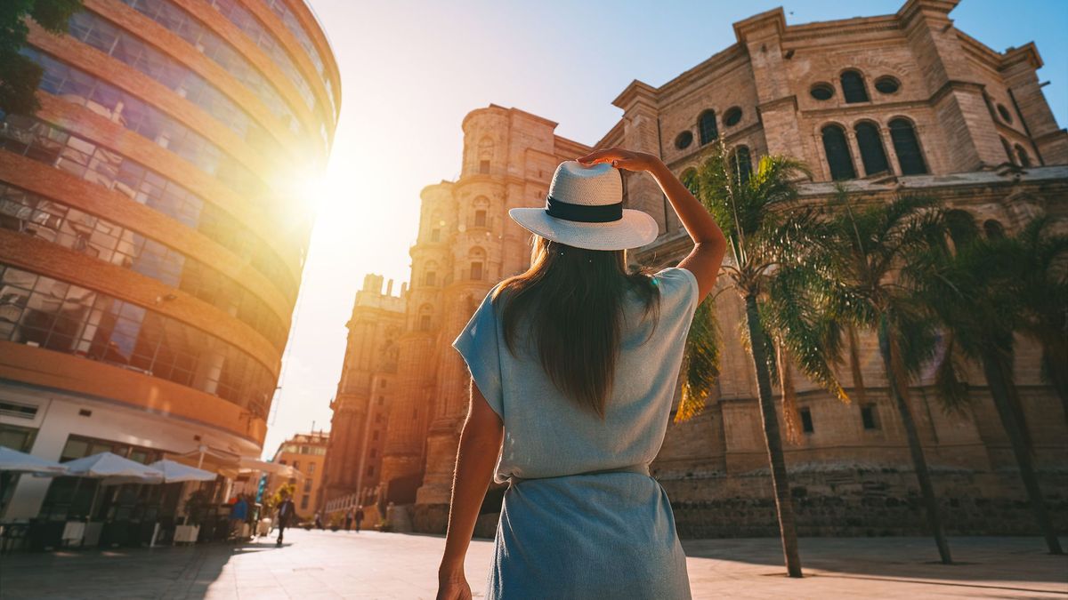 Rear view of young tourist woman in white sun hat walking in Malaga city at sunset. Summer holiday vacation in Spain