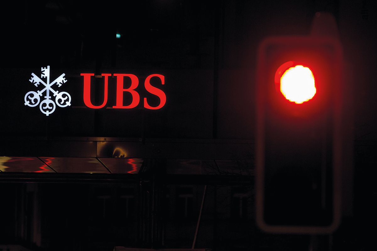 An illuminated UBS logo sits on a sign outside a bank branch, operated by UBS Group AG, near a red road traffic signal in Zurich, Switzerland, on Tuesday, Feb. 10, 2015. UBS fell after reporting lower-than-expected earnings at its wealth management division and warning that the strong franc and negative interest rates may hurt profitability. Photographer: Philipp Schmidli/Bloomberg via Getty Images, svájc, bank, svájci bank