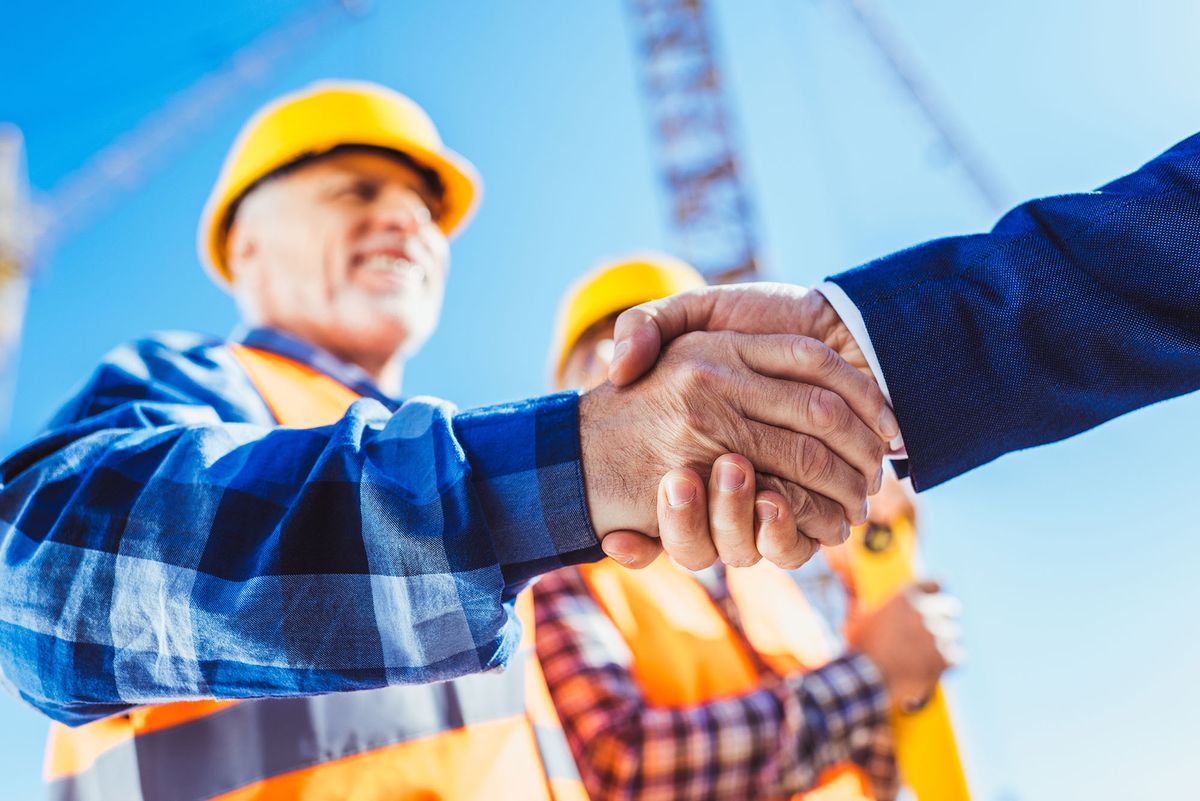 bértárgyalás állásinterjú Construction worker in protective uniform shaking hands with businessman at construction site