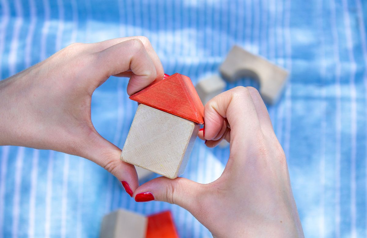 house from wooden cubes in woman's hand, red color nail, blue blanket and another eco toys in background. Mortgage property insurance, personal own home concept. copy space. buy house, insurance 