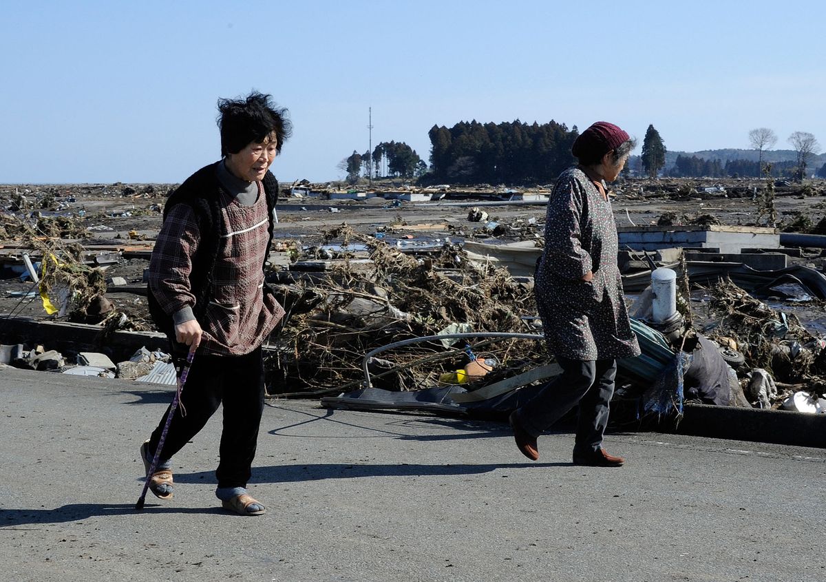 TO GO WITH AFP STORY: Japan nuclear disaster tsunami anniversary reconstruction, by Shingo ItoThis picture taken on March 12, 2011 shows local residents look at debris brought by the huge tsunami in Minamisoma, Fukushima Prefecture. Some 19,000 people were  dead and still missing after a monster tsunami unleashed by a massive quake which wreaked destruction across northeast Japan and meltdown of Fukushima Daiichi nuclear power plant.  AFP PHOTO  / TORU YAMANAKA (Photo by TORU YAMANAKA / AFP)