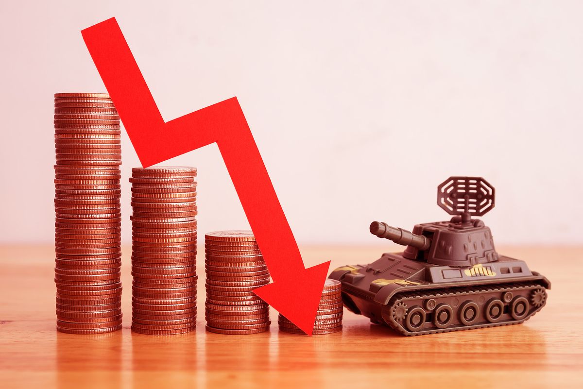 Economic crisis impact of Russian invasion of Ukraine concept. Stacked coins, graph falling down and battle tank on wooden table background copy space. War effect to world economy.