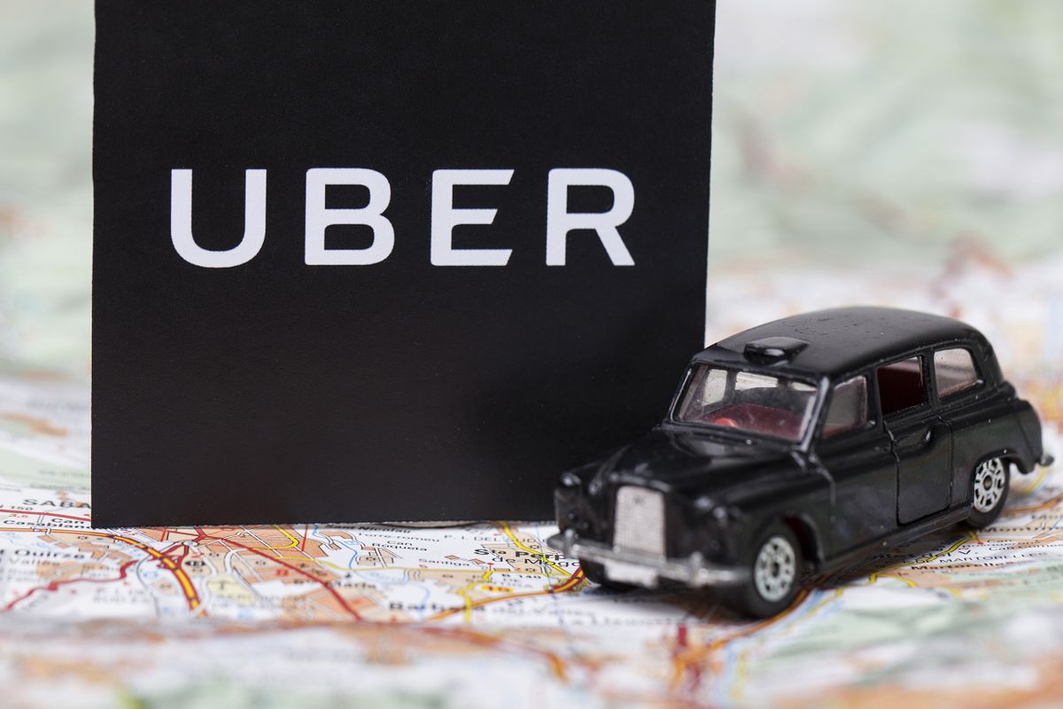 London, UK - MARCH 23rd 2017: A photograph of  the Uber logo with a black London style taxi toy car. Uber is a popular taxi style transport service application, founded in 2009