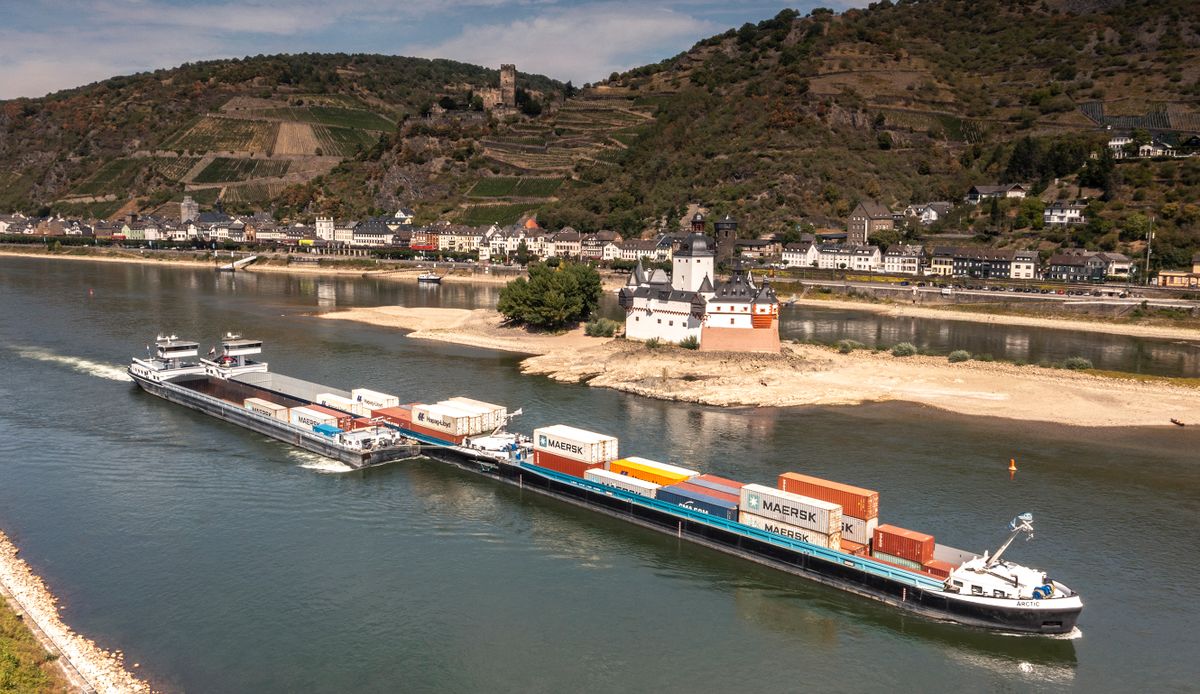 A damaged cargo ship makes its way past Burg Pfalzgrafenstein Castle (in the river) and Burg Gutenfels Castle (on the hill in background) in Kaub near Sankt Goar, western Germany, as it is towed away after suffering a technical fault, authorities said, at a time when water transport was already ailing from a drought, on August 17, 2022. - The vessel got stuck at St. Goar and Oberwesel, in between the cities of Mainz and Koblenz, causing traffic to be halted. 