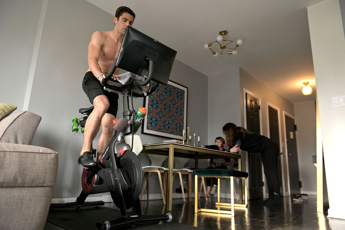 1225697666 NEW YORK, NY - MAY 18: Justin Wiezel works out on a Peloton high-tech stationary bike while his wife Marisa Wiezel (sister of photographer) homeschools their son in their apartment on May 18, 2020 in New York City. Coronavirus temporarily shut down schools and gyms, substantially increasing online education and at-home exercise routines. (Photo by Michael Loccisano/Getty Images)