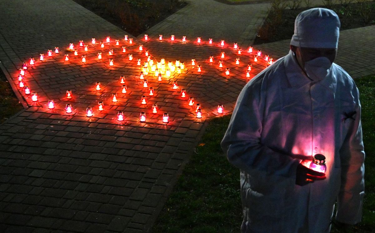 A Chernobyl plant employee holds candle near radioactivity sign at the monument to Chernobyl victims in Slavutych, the city where the power station's personnel lived, some 50 kilometres (30 miles) from the accident site on April 25, 2021, during a memorial ceremony amid the COVID-19 pandemic, caused by the novel coronavirus. - Ukraine on April 26, 2021 marks the 35th anniversary of the Chernobyl disaster which was the world's worst nuclear accident. (Photo by Sergei SUPINSKY / AFP)