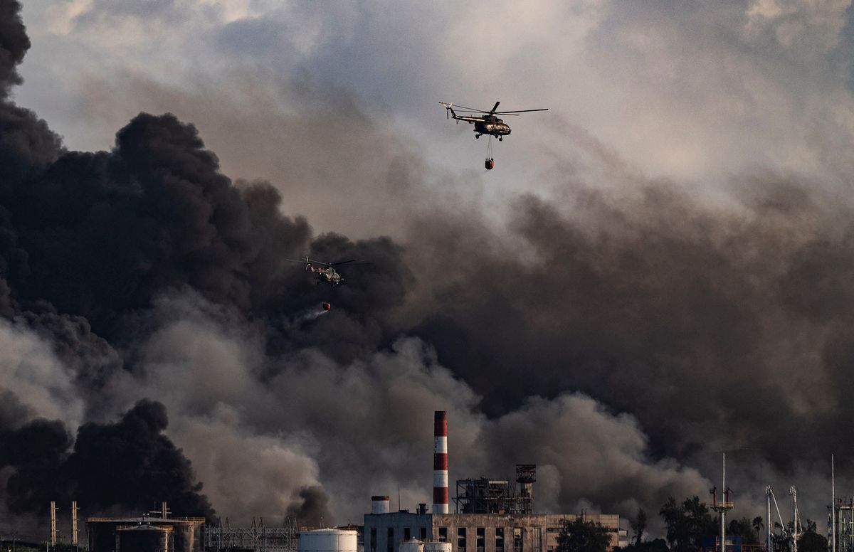 A firefighter helicopter drops water on a massive fire at a fuel depot sparked by a lightning strike in Matanzas, Cuba, on August 8, 2022. - A second oil tanker collapsed at midnight Sunday in Matanzas, in western Cuba, where firefighters have been battling a huge blaze for two days, which has left one dead and 16 missing, local authorities reported. (Photo by YAMIL LAGE / AFP)