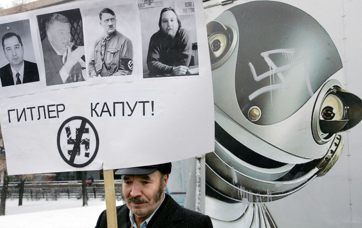 An activist of "For human rights" movement holds a banner reading "Hitler kaputt" with portraits of leaders of Motherland (Rodina) party Dmitry Rogozin (L), Liberal-Democratic Party Vladimir Zhirinovsky (2nd L), Nazi Adolf Hitler and Eurasia party Aleksandr Dugin (R) during an anti-fascism protest in Moscow, 20 November 2005 in memory of Galina Starovoitova, killed in 1998. According to the murdered deputy's assistant, Ruslan Linkov, the murdered allegedly was ordered by far right nationalists. AFP PHOTO / DENIS SINYAKOV (Photo by DENIS SINYAKOV / AFP)