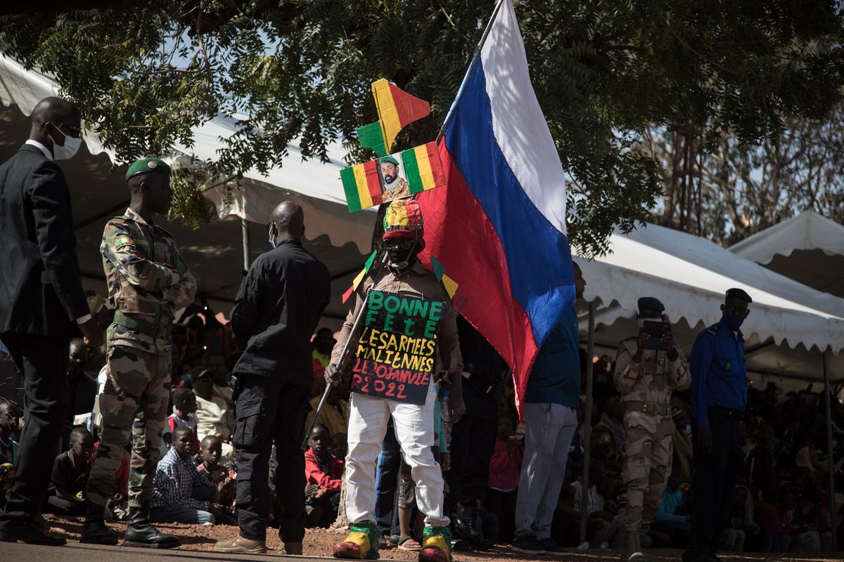 A Griot, a man specialised in praise and parody, carrying a Russian flag, a protrait of President Assimi Goďta and a sign reading "bonne fęte les armées Maliennes" (happy day to the Malian armies) parades during a ceremony celebrating the army's national day in Kati, on January 20, 2022. - With the support of French, European and Russian partners, the Malian army is trying to regain the territories occupied by armed groups and jihadists. 