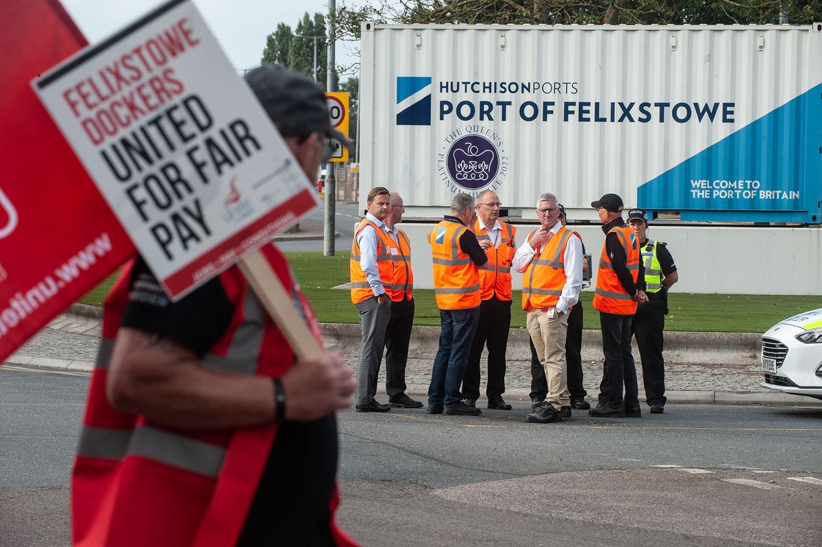 1416349726 FELIXSTOWE, SUFFOLK - AUGUST 21: Management are seen discussing the dispute with CEO Clemence Cheng (in orange vest and black baseball cap) near the main gate of Felixstowe port as an eight day strike, called by the UNITE trade union begins over pay on August 21, 2022 in Felixstowe, England. (Photo by Guy Smallman/Getty Images)