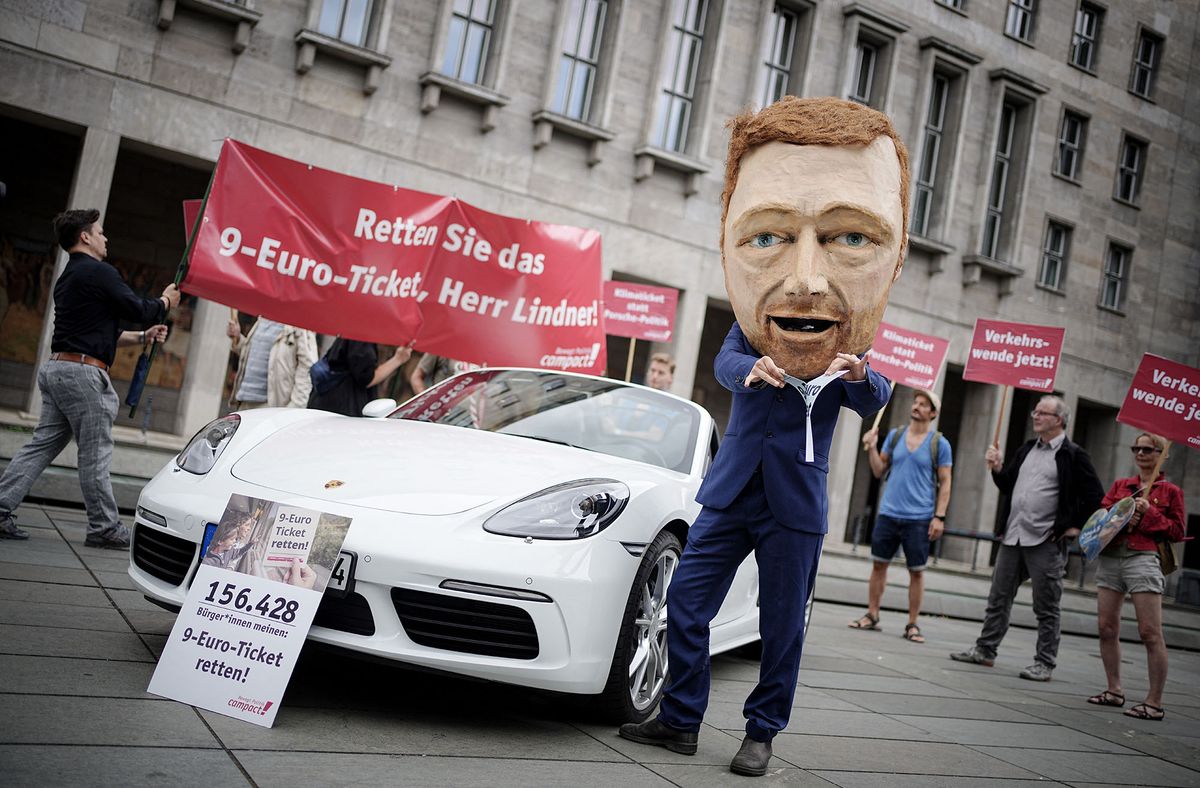 01 August 2022, Berlin: Participants and activists of the campaign organization Campact protest with banners, a Porsche and an oversized mask depicting the likeness of Finance Minister Lindner in front of the Ministry of Finance for the preservation of the 9-euro ticket. The monthly ticket for local transport is still valid until Aug. 31, 2022. Photo: Kay Nietfeld/dpa (Photo by KAY NIETFELD / DPA / dpa Picture-Alliance via AFP)