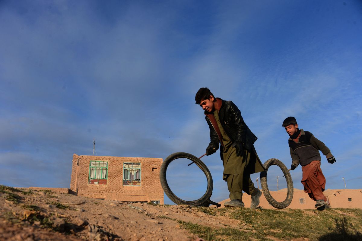 Afghan boys play with tyres along a street on the outskirts of Herat on 