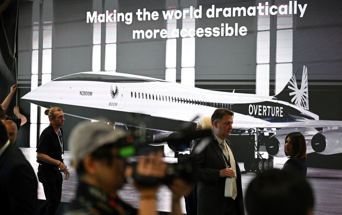 Attendees walk past a poster of a Boom Supersonic concept Overture aircraft at the Farnborough Airshow, in Farnborough, on July 18, 2022.