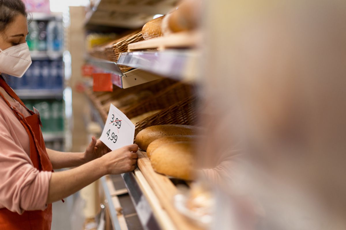Woman shop assistant changing prices of bread in supermarket, the concept of increasing inflation, A woman shop assistant changing prices of bread in supermarket, the concept of increasing inflation