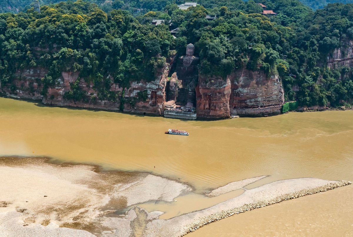 (220824) -- LESHAN, Aug. 24, 2022 (Xinhua) -- Aerial photo taken on Aug. 23, 2022 shows the exposed base of the Leshan Giant Buddha in southwest China's Sichuan Province. Facing the confluence of the Minjiang, Dadu and Qingyi rivers which saw the decrease of water level in recent days due to continuous high temperature, the base of the Leshan Giant Buddha became exposed above the water. (Xinhua/Shen Bohan) (Photo by Shen Bohan / XINHUA / Xinhua via AFP)