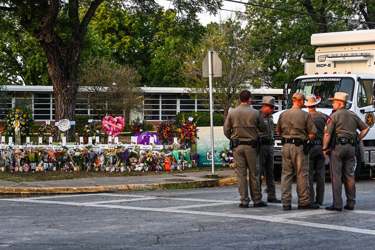 Police officers speak near a makeshift memorial for the shooting victims outside Robb Elementary School in Uvalde, Texas, on May 27, 2022. - Texas police faced angry questions May 26, 2022 over why it took an hour to neutralize the gunman who murdered 19 small children and two teachers in Uvalde, as video emerged of desperate parents begging officers to storm the school. (Photo by CHANDAN KHANNA / AFP)