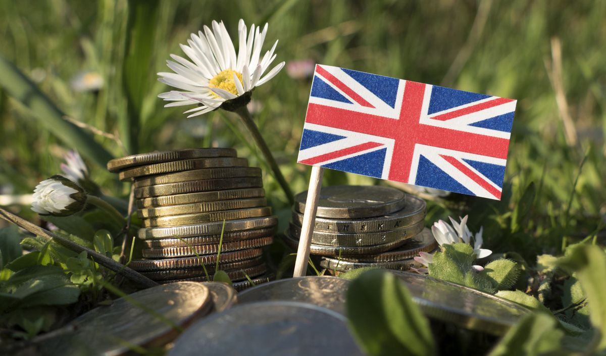 United,Kingdom,Flag,With,Stack,Of,Money,Coins,With,Grass