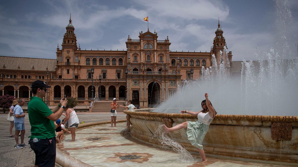People cool off with a fountain's water during a heatwave in Seville on July 12, 2022. - Firefighters battled wildfires in Spain and Portugal as Western Europe faced its second heatwave in less than a month which threatened glaciers in the Alps and worsened drought conditions. The mass of hot air which pushed temperatures above 40 degrees Celsius (104 Fahrenheit) in large parts of the Iberian Peninsula was set to spread to the north and east in the coming days. (Photo by JORGE GUERRERO / AFP)