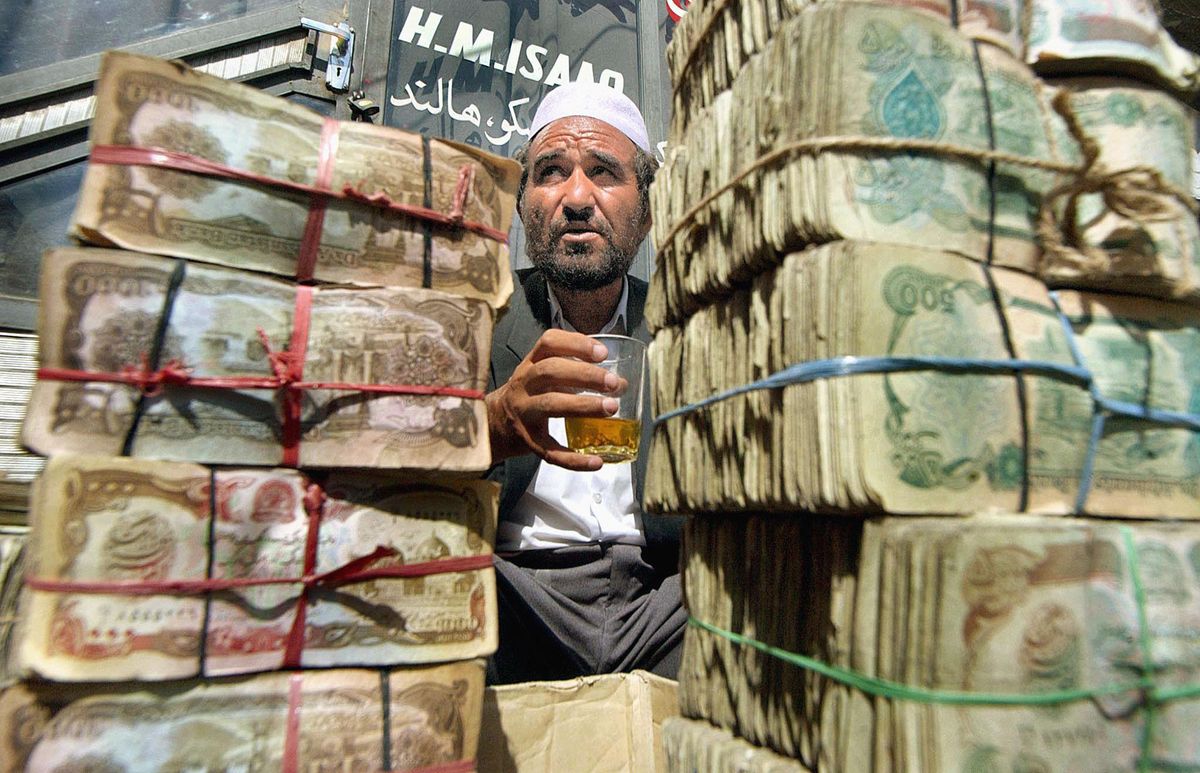 Abdul Aziz, an elder Afghan money changer, takes a break sitting behind bundles of afghanis at the main currency exchange market in Kabul, 18 July 2002.  Stacks of bank notes are spread at the feet of money changers at the Kabul bazaar, who after having made trade under all the different regimes who have ruled the country over the past 30 years, hope the current leaders one will bring stability to the economy.  AFP PHOTO/JEWEL SAMAD (Photo by JEWEL SAMAD / AFP)