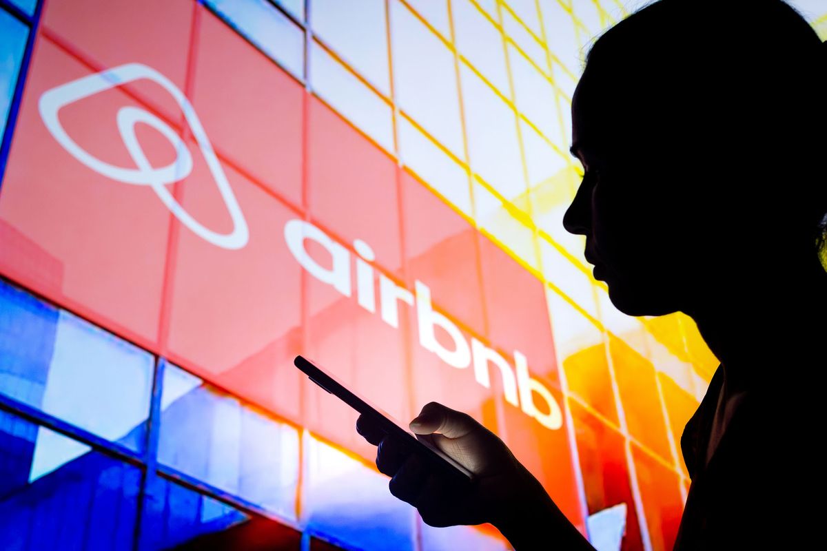 1239628130 BRAZIL - 2022/03/30: In this photo illustration, a woman's silhouette holds a smartphone with the Airbnb logo in the background. (Photo Illustration by Rafael Henrique/SOPA Images/LightRocket via Getty Images)