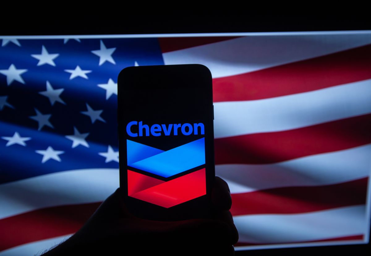 Dow Jones Major Stock Companies, The logo of the American oil campany Chevron is seen on a screen in front of an American flag. It is listed in the Dow Jones as it is one of the major US companies on the stock market. (Photo by Alexander Pohl/NurPhoto via Getty Images)