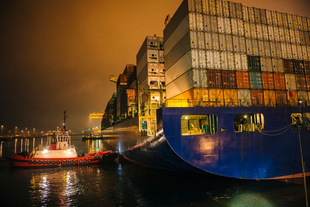 Tugboat manoeuvring container ship on river at night, Tacoma, Washington, USA (Photo by Pete Saloutos / Image Source / Image Source via AFP) konténerhajó, tengeri kereskedelem