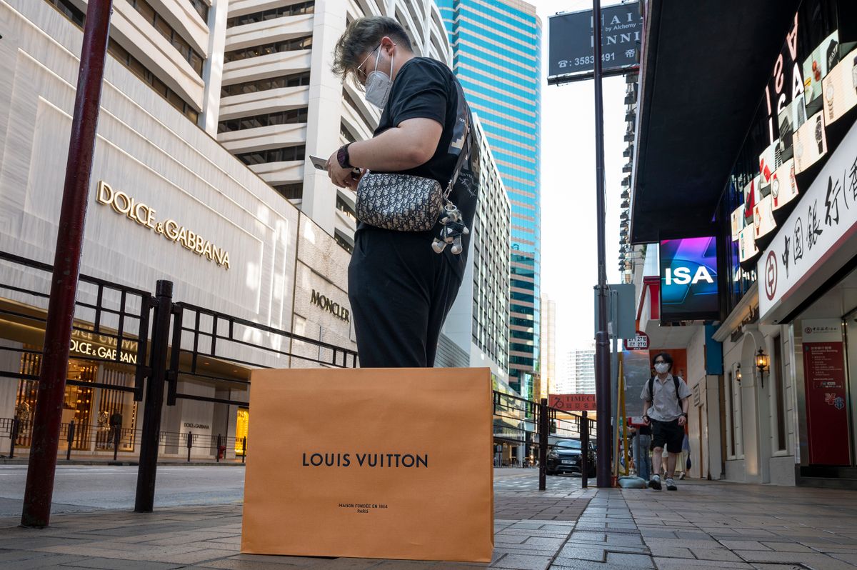 HONG KONG, CHINA - 2022/09/29: A male customer uses a smartphone next to a Louis Vuitton shopping bag in front of the Italian luxury fashion house Dolce & Gabbana store in Hong Kong.
