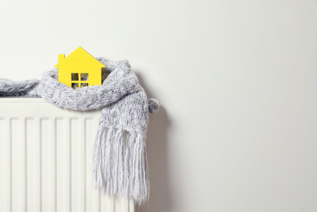House,Model,Wrapped,In,Scarf,On,Radiator,Indoors,,Space,For House model wrapped in scarf on radiator indoors, space for text. Winter heating efficiency House model wrapped in scarf on radiator indoors, space for text. Winter heating efficiency
