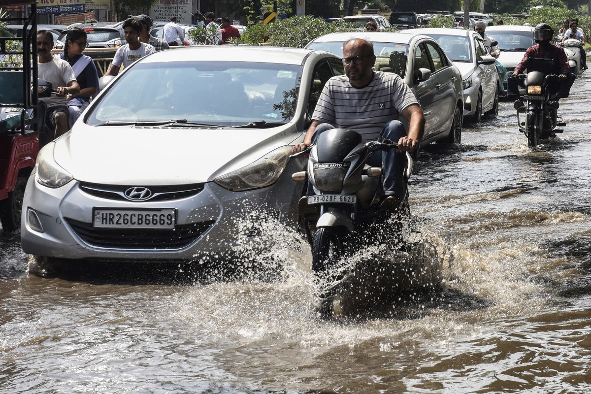 Commuters make their way along a waterlogged road after a heavy rainfall in Amritsar on August 30, 2022. 