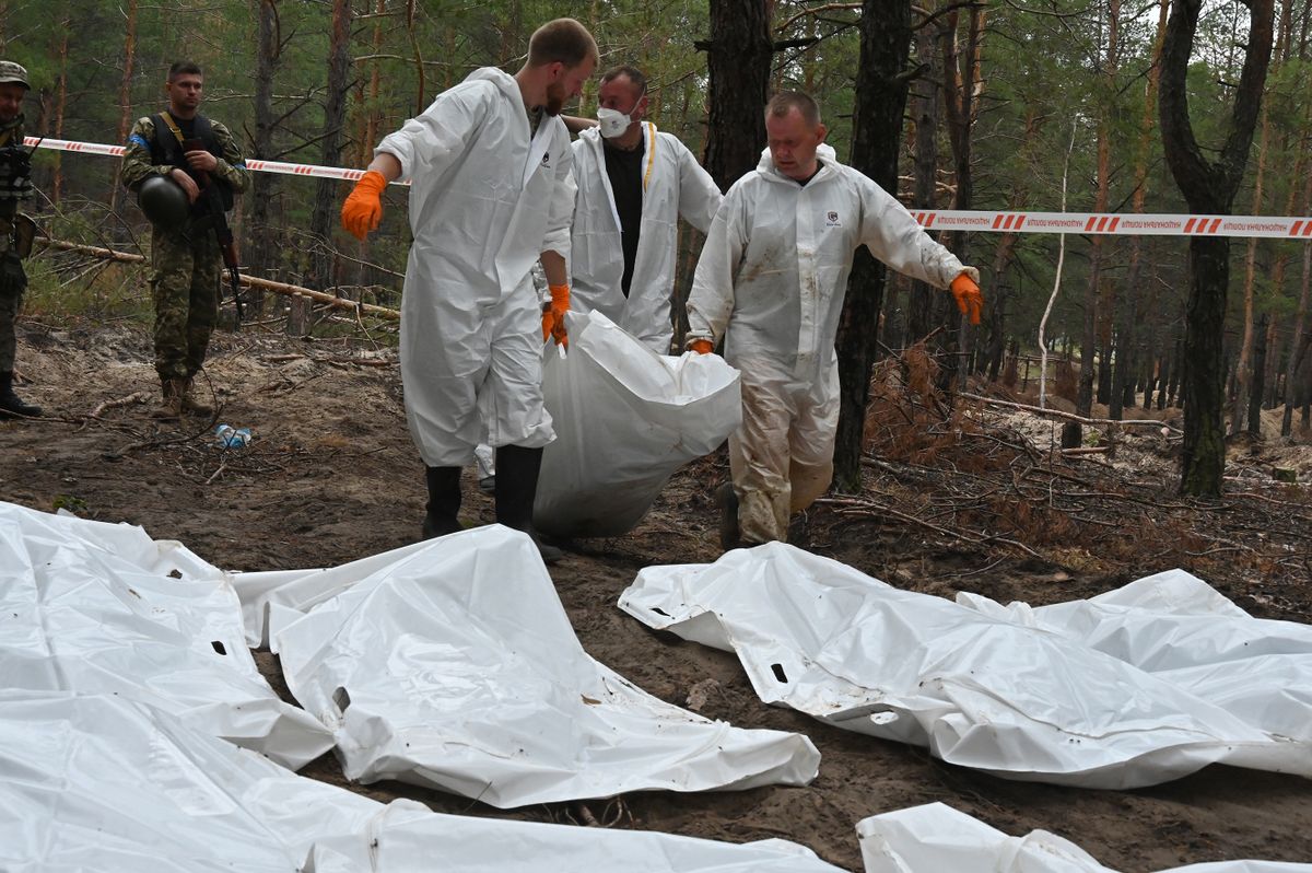 Forensic technicians carry a body bag in a forest on the outskirts of Izyum, eastern Ukraine on September 16, 2022. - Ukraine said on September 16, 2022 it had counted 450 graves at just one burial site near Izyum after recapturing the eastern city from the Russians. 