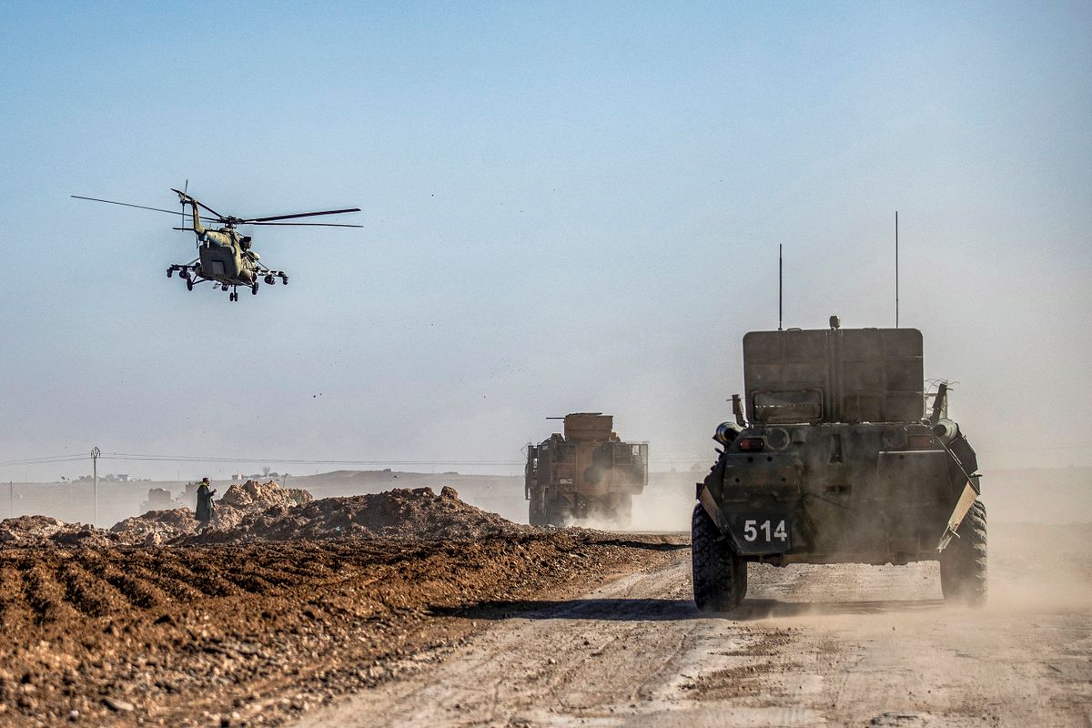 A Russian Mil Mi-17 military helicopter flies by military vehicles driving in a joint Russian-Turkish patrol convoy in the eastern countryside of the town of Darbasiyah near the border with Turkey in Syria's northeastern Hasakah province on December 7, 2020. 