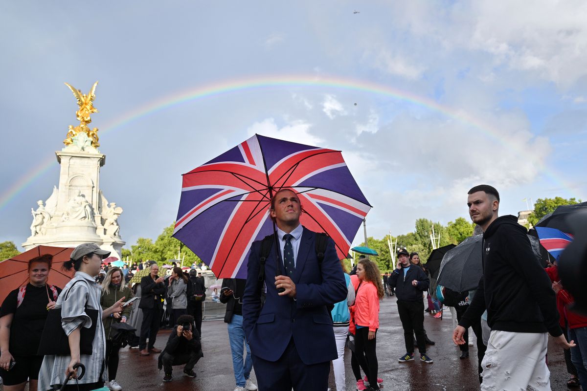 LONDON, ENGLAND - SEPTEMBER 08: A man looks on holding a Union flag umbrella as a rainbow is seen outside of Buckingham Palace on September 08, 2022 in London, England. Buckingham Palace issued a statement earlier today saying that Queen Elizabeth was placed under medical supervision due to concerns about her health. 