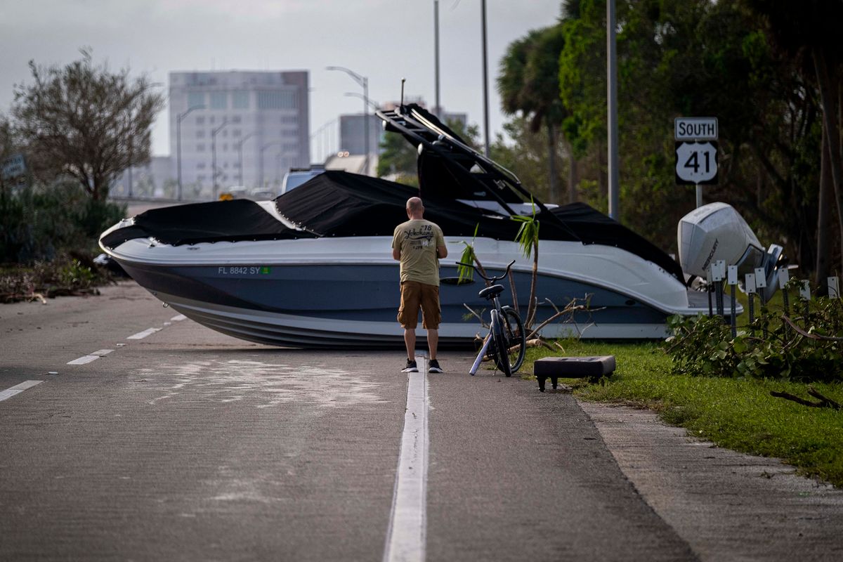 A man stands in front of a washed boat in the aftermath of Hurricane Ian in Fort Myers, Florida on September 29, 2022. - Hurricane Ian left much of coastal southwest Florida in darkness early on Thursday, bringing "catastrophic" flooding that left officials readying a huge emergency response to a storm of rare intensity. The National Hurricane Center said the eye of the "extremely dangerous" hurricane made landfall just after 3:00 pm (1900 GMT) on the barrier island of Cayo Costa, west of the city of Fort Myers. 