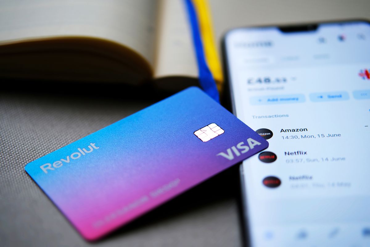 Stone,/,Uk,-,July,8,2020:,New,Redesigned,Revolut Stone / UK - July 8 2020: New redesigned Revolut Bank card placed on top of smartphone with Revolut app showing the balance on the screen. Selective focus. Main focus is on the chip and logo. Stone / UK - July 8 2020: New redesigned Revolut Bank card placed on top of smartphone with Revolut app showing the balance on the screen. Selective focus. Main focus is on the chip and logo.
