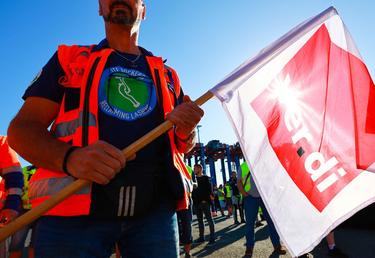 Hamburg - Warning strike dockers, 14 July 2022, Hamburg: A worker with the logo of the ITF - International Transport Workers' Federation on his T-shirt, holds a Verdi flag during a warning strike in front of the Container Terminal Burchardkai (CTA) of HHLA (Hamburger Hafen und Logistik AG). There is still no agreement in sight in the conflict over pay for port workers at Germany's major North Sea ports. The Verdi trade union has called on seaport workers to go on a 48-hour warning strike. Photo: Christian Charisius/dpa (Photo by CHRISTIAN CHARISIUS / DPA / dpa Picture-Alliance via AFP)