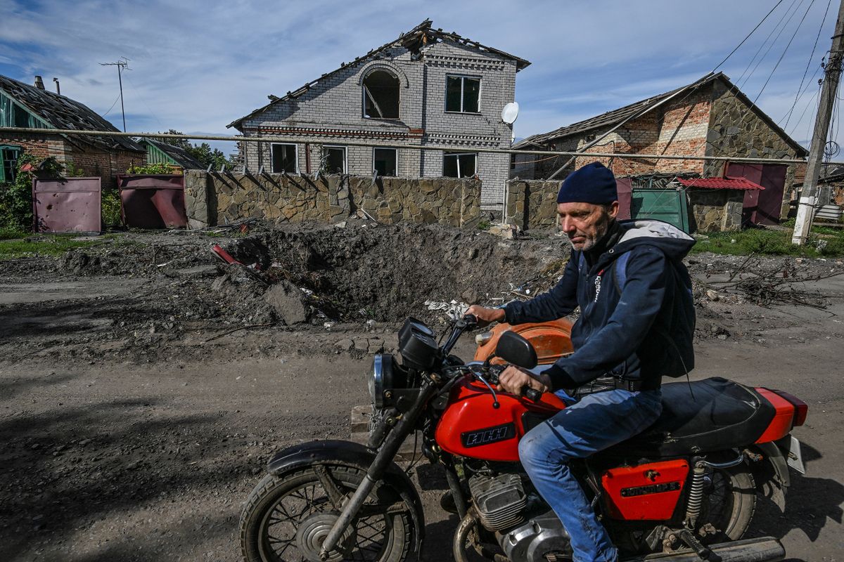 A man rides a motorbike past damaged houses and a crater in the ground in Siversk, Donetsk region, on September 20, 2022, amid Russia's military invasion on on Ukraine. 