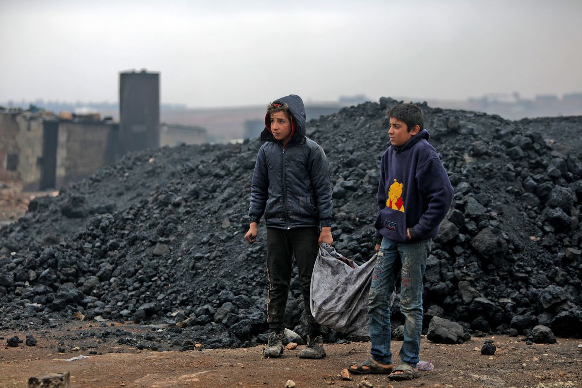 Syrian boys transport coal as they work at a makeshift oil refinery near the Turkish-controlled northern city of al-Bab, on November 20, 2021. - After a decade of war, an estimated 2.5 million children in Syria are out of school with another 1.6 million at risk of dropping out, according to the UN's children agency UNICEF. As it marked World Children's Day on November 20, the agency estimated that nine in ten children live in poverty and more than 5,700 children – some as young as seven – were recruited into the fighting. 