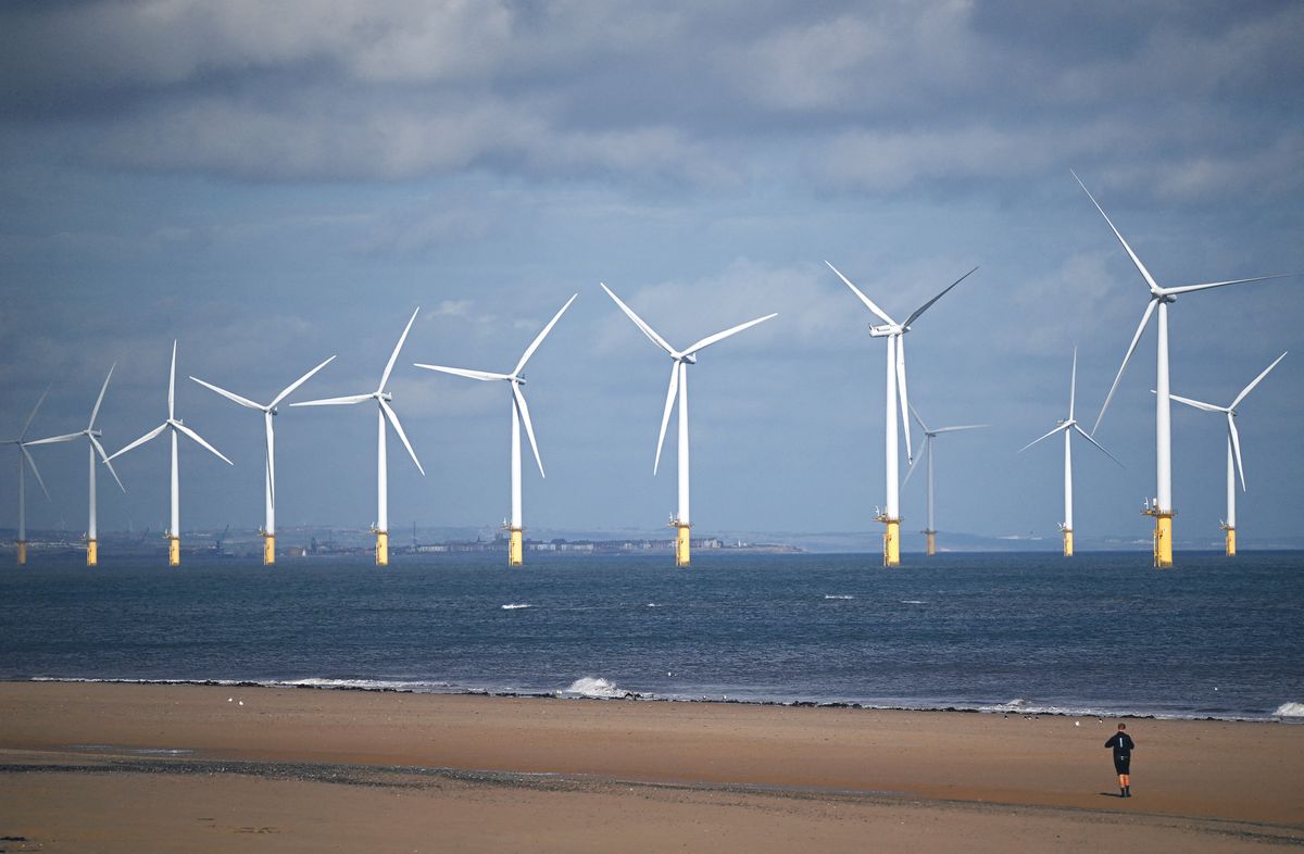A person walks along the beach backdropped by wind turbines of EDF Energy Renewables' Teesside Wind Farm, off the coast of Redcar in north east England on September 7, 2022. - Britain's new Prime Minister Liz Truss is getting down to business fast with plans for a big-spending offensive to rein in soaring energy prices, putting her on collision course with nervous financial markets. (Photo by Oli SCARFF / AFP)