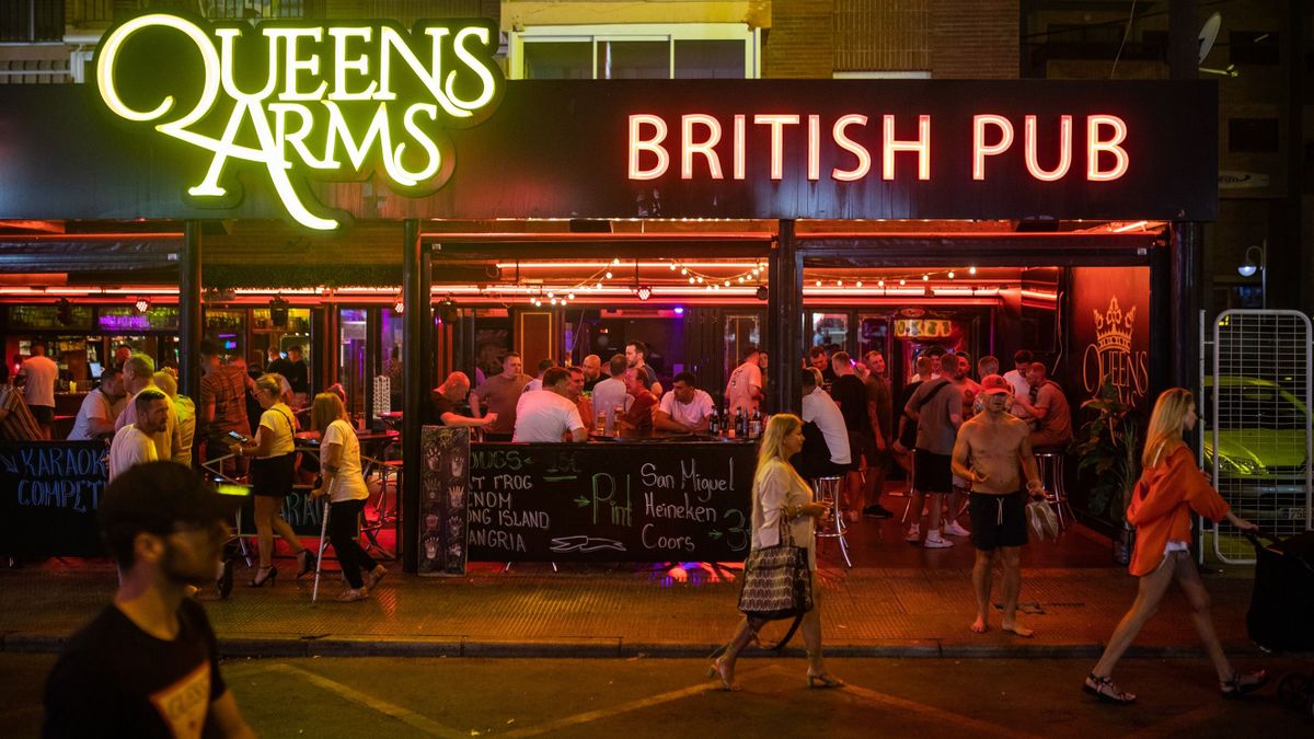 BENIDORM, SPAIN - SEPTEMBER 10: English tourists stroll through the nightlife area in front of the Queen Isabell II themed Queens Arms Benidorm bar on September 10, 2022 in Benidorm, Spain. Queen Elizabeth II died at Balmoral Castle in Scotland on September 8, 2022, and is succeeded by her eldest son, King Charles III. 