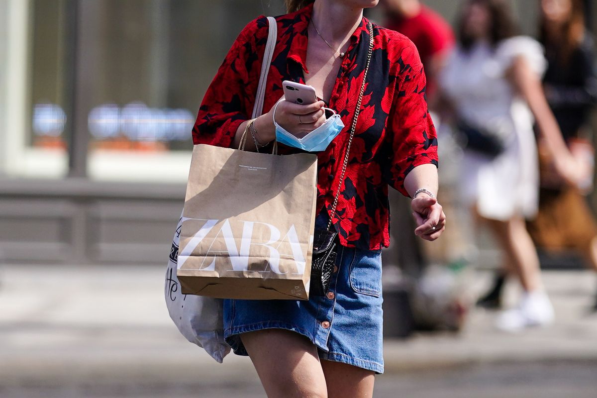 Street Style In Paris - July 2020, PARIS, FRANCE - JULY 11: A passerby wears a red floral print shirt, a blue denim skirt, holds a brown paper Zara shopping bag, holds a mobile phone "Iphone" from Apple and a blue protective face mask, on July 11, 2020 in Paris, France. (Photo by Edward Berthelot/Getty Images)
