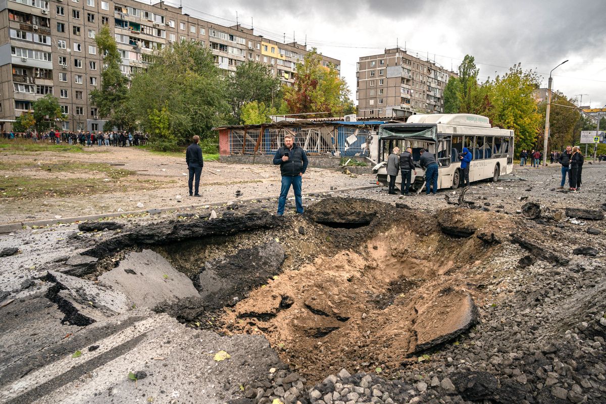 Investigators examine a crater and a damaged bus, following a missile strike in Dnipro on October 10, 2022, amid Russia's invasion of Ukraine. - The head of the Ukrainian military said that Russian forces launched at least 75 missiles at Ukraine on Monday morning, with fatal strikes targeting the capital Kyiv, and cities in the south and west. (Photo by Dimitar DILKOFF / AFP)